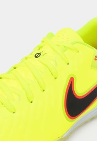 Zapatilla deportiva de color amarillo brillante con el logo de Nike en negro y rojo, cordones amarillos y un pequeño logo negro cerca del agujero del cordón superior.