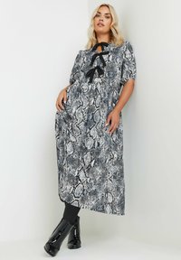 Mustekka-valkoinen käärmeennahkakuosiset mekko, jossa on avainaukko kaula-aukko ja nauhatyyli, lyhyet hihat ja rento malli, yhdistettynä mustiin kiiltäviin saappaisiin.