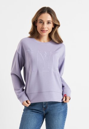 Paarse sweater met "NYC" in verhoogde letters, lange mouwen, geribde manchetten en een relaxte pasvorm. De stof lijkt zacht en glad te zijn.
