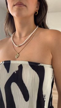 Svart och vit plisserad strapless-topp med ett vågigt mönster, parat med ett lagerhalsband av pärlor och guld accenter, samt hoops örhängen.