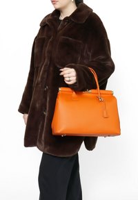 Bruine faux bontjas met grote zakken, gecombineerd met een oranje leren handtas met een gestructureerde vorm en gouden hardware accenten.
