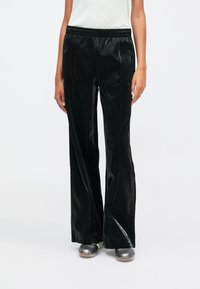 Μαύρα, γυαλιστερά παντελόνια με φαρδιά μπατζάκια, ελαστική μέση, πλαϊνές τσέπες και διακριτές κάθετες ραφές. Λείο υφή σε όλη την επιφάνεια.