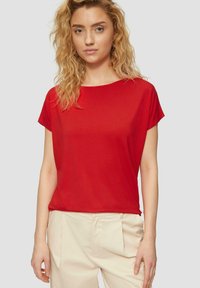 Rotes Kurzarm-T-Shirt aus weichem Stoff mit Rundhalsausschnitt und lockerer Passform, kombiniert mit cremefarbenen Hosen für einen Kontrast.