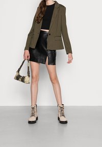 Olivově zelené sako přes černý crop top, doplněné černou koženou minisukní s předním rozparkem. Béžové šněrovací combat boty a kabelka s hadím vzorem.