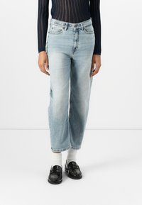 Jeans in denim leggermente blu con una vestibilità rilassata, dotati di una vita alta, tasche frontali e una lunghezza leggermente accorciata. Indossati con mocassini neri.