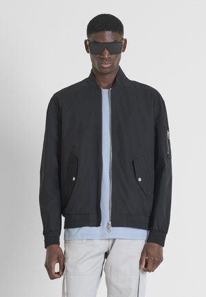 Black bomber jacket with a stand collar, front zip, and two side pockets. Features a zippered sleeve pocket and soft texture.