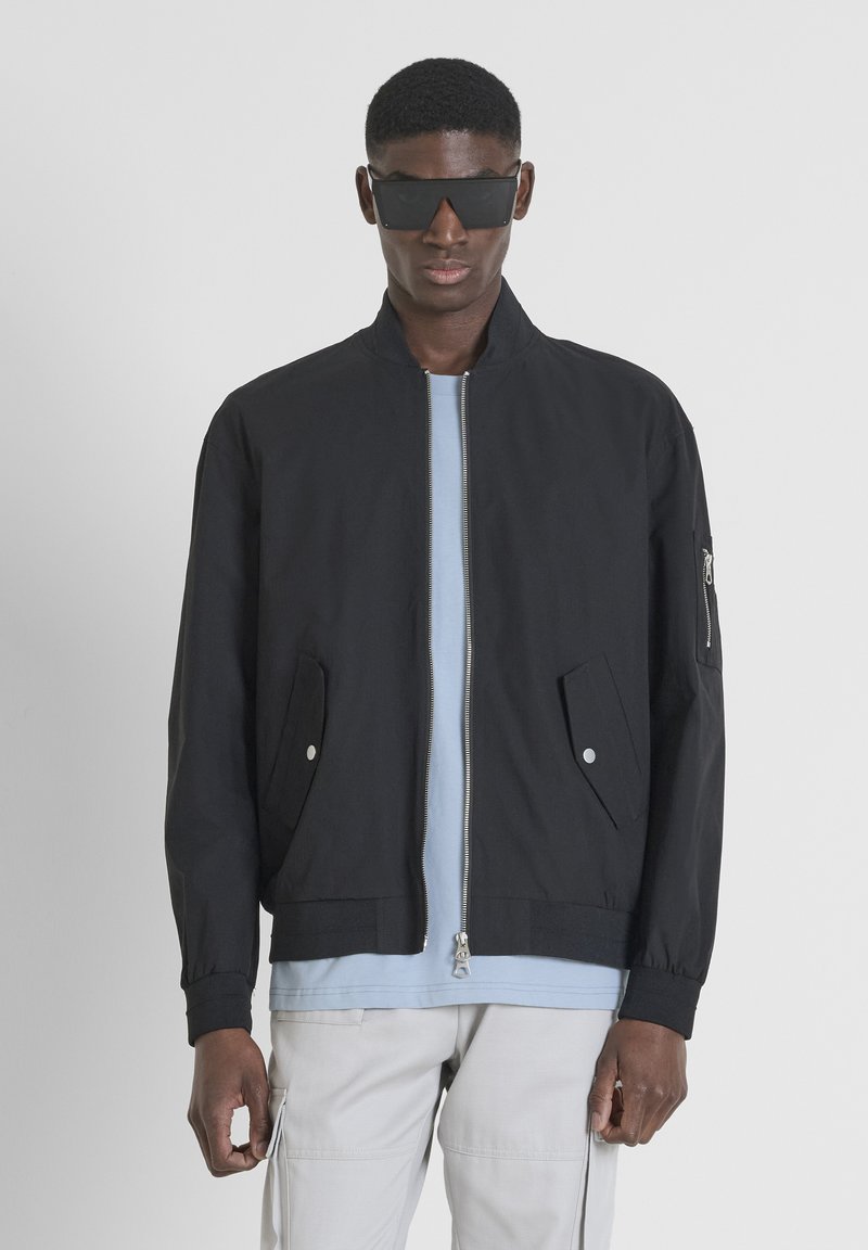 Giubbotto bomber nero con collo rialzato, zip frontale e due tasche laterali. Presenta una tasca con zip sulla manica e una texture morbida.