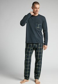 Mörkblå långärmad topp med bröstficka; matchande rutiga byxor i mörkblått med gult rutmönster; bomullstyg; avslappnad passform; modell barfota.