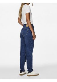 Mörkblå högmidjade jeans med avslappnad passform, utrustade med bakfickor och en läderlapp på midjebandet, tillsammans med en vit t-shirt.