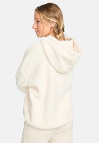 Fluffy witte hoodie met een relaxte pasvorm, zachte textuur en een grote capuchon, weergegeven van achteren.
