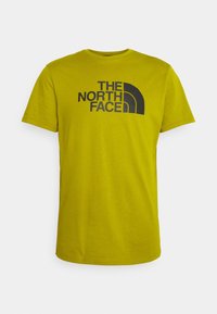 Gele T-shirt met korte mouwen van katoen, met een zwarte logo-opdruk van "THE NORTH FACE" op de voorkant in een vet lettertype. Ronde hals.