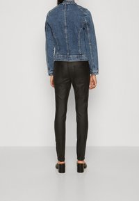 Jeansjacka i medelblått, med en figursydd design och synliga sömdetaljer, i kombination med svarta slim-fit-byxor och klackskor.