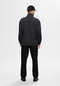 Grå sweatshirt med hög krage, svarta byxor och svart keps. Slät textur, avslappnad passform och minimalistisk design. Inga synliga mönster.