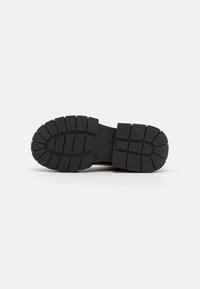 Black rubber outsole with deep treads for traction, featuring a flat design and slight ridges along the sides. Smooth center section.