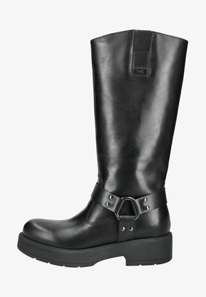 Botte en cuir noir montant jusqu'au genou avec une semelle plate, dotée d'une sangle au niveau de la cheville et d'un dispositif circulaire. Texture lisse avec un minimum de détails de couture.