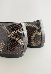 Des chaussures à imprimé serpent texturé marron et beige sont présentées de l'arrière, mettant en avant le design et la finition lisse du matériau.