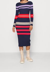 Abito midi a coste con righe verticali in navy, rosso, beige e viola. Maniche lunghe e scollo rotondo. Indossato con stivaletti beige alla caviglia.
