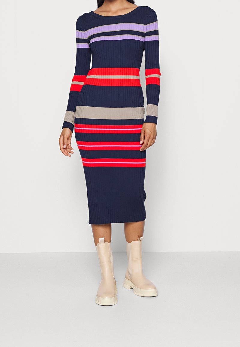 Abito midi a coste con righe verticali in navy, rosso, beige e viola. Maniche lunghe e scollo rotondo. Indossato con stivaletti beige alla caviglia.