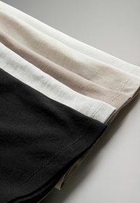 Trois morceaux de tissu en coton pliés, en noir, blanc et beige, disposés en une pile ordonnée et superposée sur une surface claire.