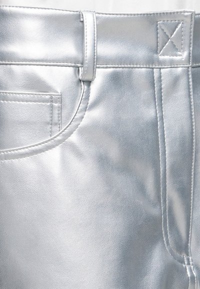 Gros plan d'un pantalon métallique argenté montrant la poche, le passants de ceinture et les détails des coutures sur un tissu brillant.