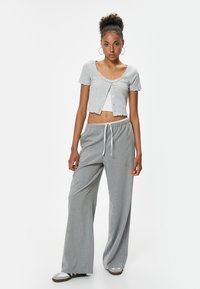 Cárdigan gris de mangas cortas con canalé y un corte cropped, combinado con pantalones de pierna ancha gris con rayas finas que cuentan con una cintura elástica y cordón.
