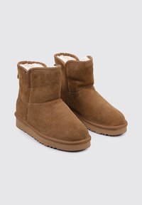 Botas cortas de ante marrón con un forro blanco suave, punta redonda y suela de goma plana con dibujo texturizado para mayor agarre.