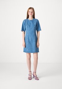 Denimmekko lyhyillä hihoilla, tiukka vartalo ja suora helma. Vaaleansininen väri, jossa on erottuvaompelua ja repaleiset reunat.