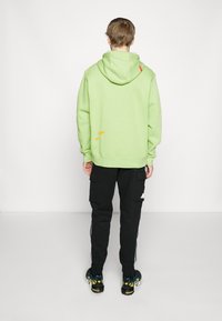 Ljusgrön hoodie med en frontficka och en orange detalj. Kombinerad med svarta cargo byxor med sidofickor. Svarta och färgglada sneakers.