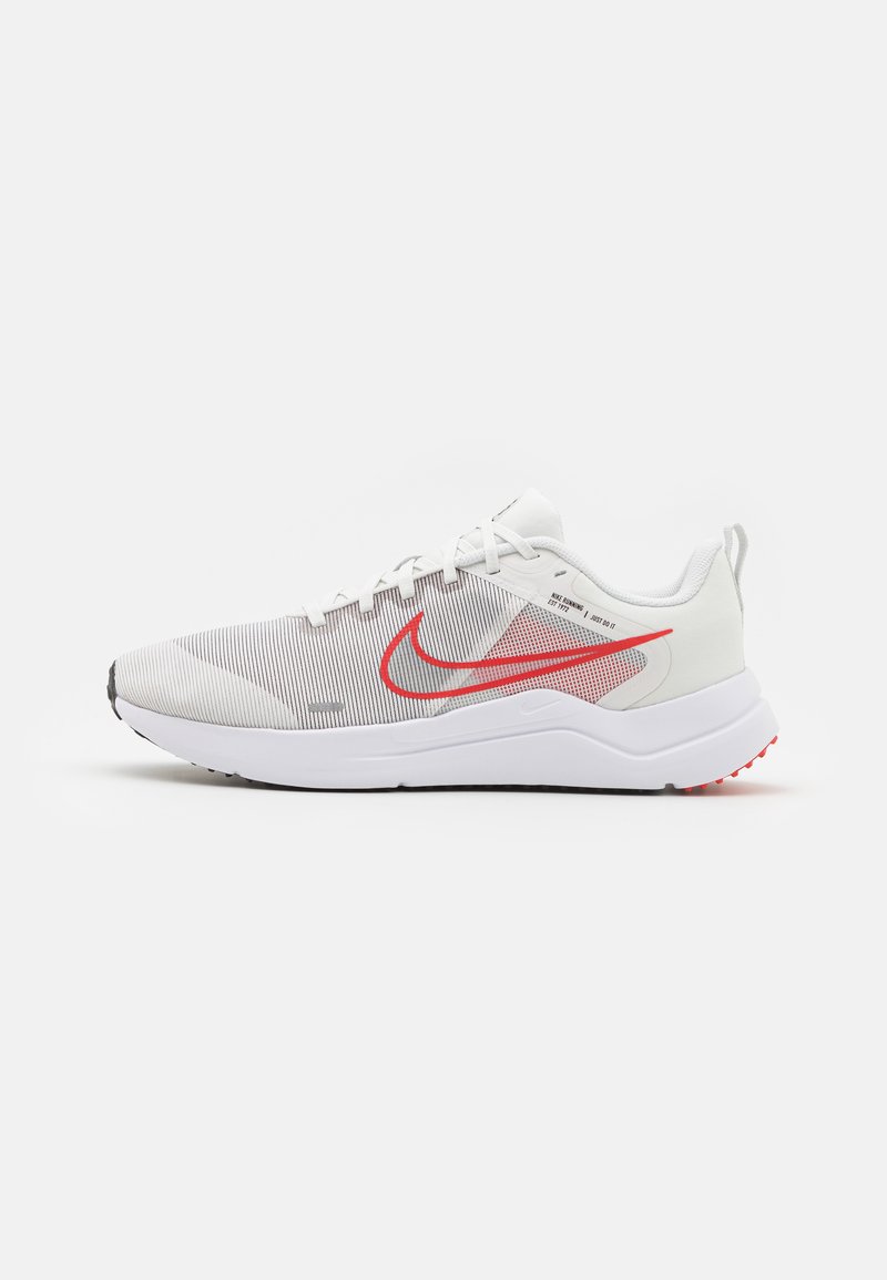 Weiße Sport Schuhe mit einem strukturierten Mesh-Obermaterial, ausgestattet mit einem roten Nike-Swoosh und grauen Akzenten. Die Sohle ist gepolstert und hat ein schwarzes Profil.
