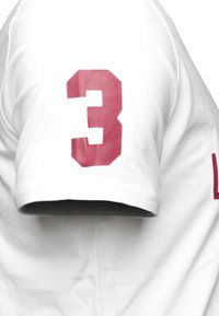 Valkoinen puuvillainen t-paita, jossa on suuri punainen numero "3" painettuna vasempaan hihaan. Klassinen pyöreä kaula-aukko ja lyhyet hihat.