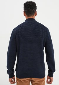 Marineblauer Strickpullover mit strukturiertem Muster an den Schultern, gerippten Ärmelbündchen und Saum. Hergestellt aus weichem Stoff mit lockerer Passform.