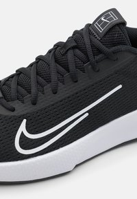 Černé tenisky Nike s textilním svrškem a bílým logem swoosh. Mají šněrování, texturovaný povrch a kontrastní bílou mezipodešev.