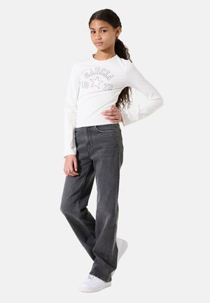 Weißes Langarmshirt mit dem Druck "GARCA 1972", kombiniert mit lockeren grauen Jeans und weißen Sneakers, vor einem schlichten Hintergrund.