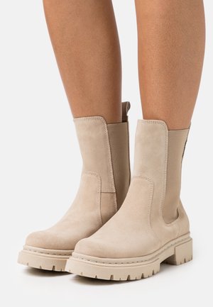 Beige suede ankle boots with elastic side panels, square toe, chunky rubber sole, and serrated tread for traction.