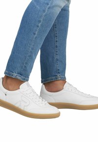 Vita lädersneakers med en låg profil, strukturerad gummisula och snörning. Matchas med ljusblå jeans.