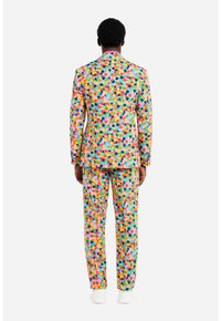 Abito colorato con giacca aderente e pantaloni abbinati, caratterizzato da un motivo a pois in tonalità di rosa, giallo, blu e verde.