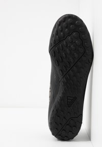 Suela de zapato atlético negro con superficie de goma texturizada, que presenta patrones redondos y ovalados, además de un logo grabado.