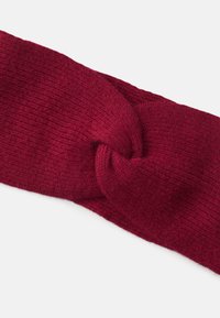 Rød strikket pandebånd med et snoet design foran. Teksturen er blød og ribbet, hvilket tilføjer visuel interesse til accessoiret.