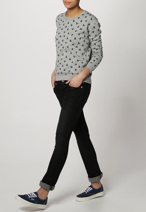 Felpa grigia con piccoli motivi neri, abbinata a jeans neri aderenti e sneakers blu scuro. Design casual con polsini a coste.