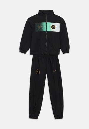 Survêtement noir avec veste zippée et pantalon, avec un panneau vert et blanc sur la poitrine avec des logos et un marquage doré Nike et KM.