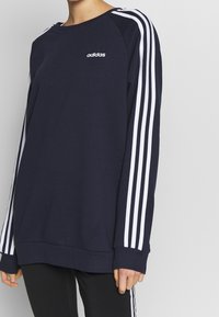 Sudadera azul marino con detalles de tres rayas blancas en las mangas y un cuello redondo. Material suave con un corte relajado y logo bordado.