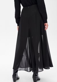 Zwarte maxi rok van transparant materiaal met een vloeiende uitstraling, voorzien van een subtiele plooi in de taille en zijsplitten voor extra beweging.