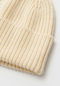 Berretto a coste color crema, caratterizzato da una morbida texture simile alla lana e da un risvolto piegato. Dettagli sottili ne valorizzano il design classico.