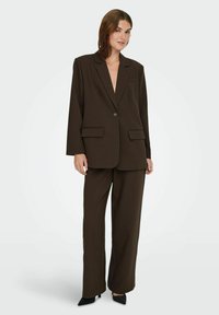 Brauner maßgeschneiderter Blazer mit Schalkragen, einem einzelnen Knopfverschluss und zwei Fronttaschen, kombiniert mit passenden weiten Hosen.