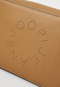 Sacca in pelle tan con una superficie texture. Presenta un design con lettering perforato e una cucitura a contrasto lungo i bordi.