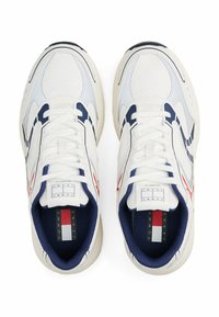 Sneaker bianche con tomaia in mesh e pelle, dettagli in blu navy, elementi rossi e suola in gomma spessa. L'interno presenta un'etichetta con il logo del marchio.