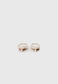 Beige slip-on sko med lav, tynn hæl. Har en glatt tekstur, åpen bakdel og kryssremmer på overdelen.