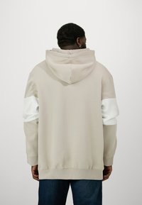 Hellbeige Kapuzenpullover mit Kapuze, kontrastierenden weißen Ärmeln und gerippten Bündchen. Glatte Stofftextur mit lockerer Passform und einem Bündchen am Saum.