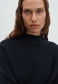 Maglione a costine blu navy scuro con collo alto, caratterizzato da un motivo lavorato a maglia testurizzato e una vestibilità morbida. Il tessuto appare morbido e accogliente.