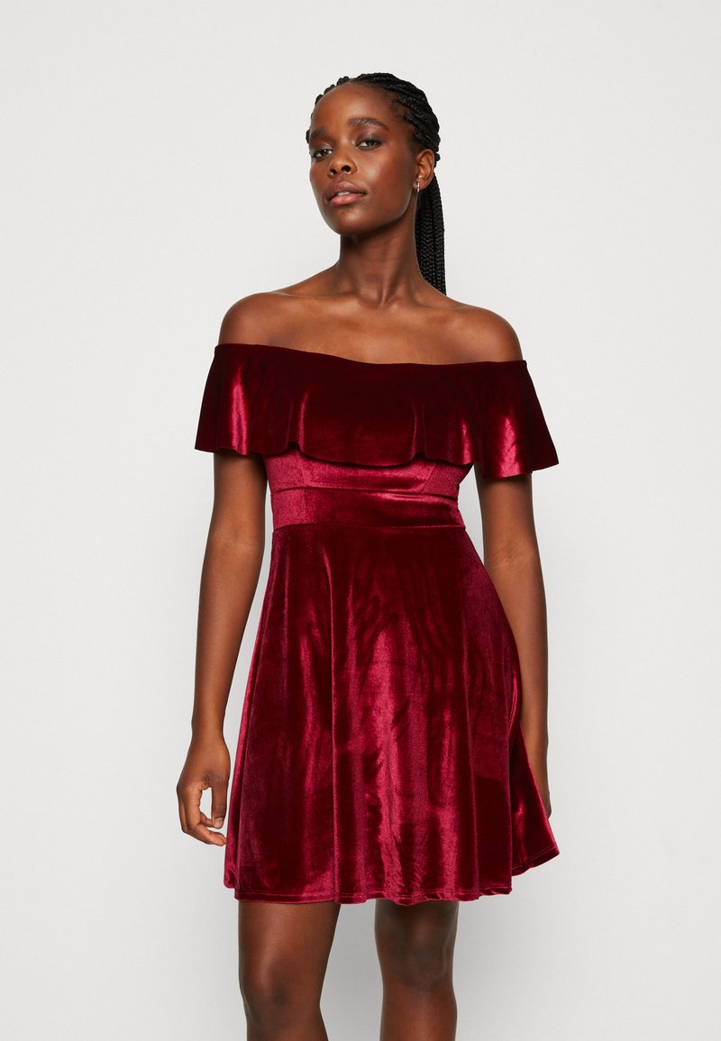 Burgundské off-shoulder šaty z jemného zamatového materiálu. Obsahujú priliehavú korzetovú časť, rozšírenú sukňu a volánikový výstrih. Hladká textúra po celej ploche.